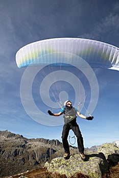 Paraglider pilot stands on a rock and balances his paraglider above his head near Lake Grimsel in the Swiss Alps