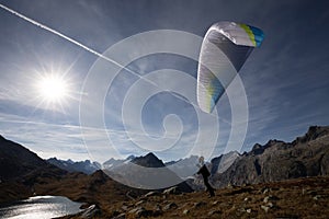 Paraglider Pilot stands on a slope and balances his paraglider above his head in the Alps of Switzerland