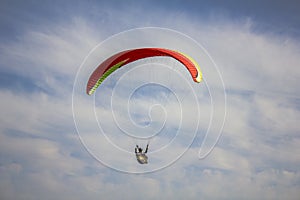 Paraglider on a red with yellow stripes paraglider flies in a blue sky with white clouds