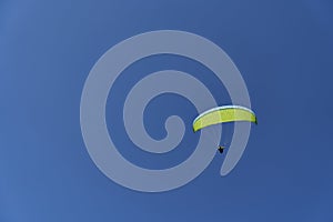 A paraglider sailing across a blue sky.