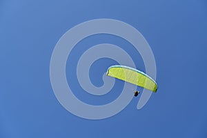 A paraglider sailing across a blue sky.