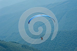 Paraglider flies over a mountain valley on a sunny summer day.