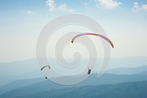 Two paragliders fly over a mountain valley on a sunny summer day.