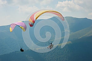 Two paragliders fly over a mountain valley on a sunny summer day.