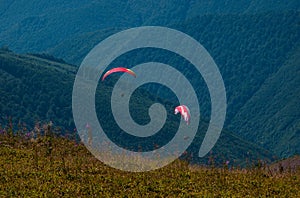 Two paragliders fly over a mountain valley on a sunny summer day.