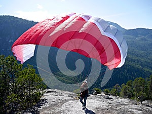 Paragliding. Woman with a red paraglider on the top of the mountain.