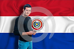 Paraguai flag on the background of the texture. The young man smiles and holds a smartphone in his hand. The concept of design photo