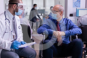 Paralized old man in wheelchair with protection mask listening doctor photo