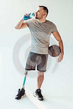 paralympic basketball player with basketball ball drinking water from sportive bottle