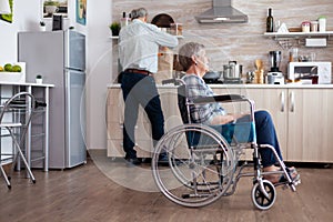 Paralysed senior woman in wheelchair feeling unhappy in kitchen photo