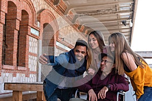 Paralytic man in a wheelchair accompanied by a young man and a girls taking a photo with their mobile