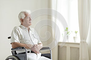 Paralyzed, elderly man in a wheelchair alone in a room