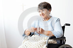 Paralyzed senior woman in a wheelchair praying to god