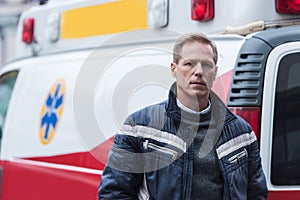 paramedic in casual clothes standing in front of ambulance and looking