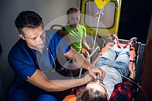 A paramedic puts on an oxygen mask on an unconscious woman lying on a stretcher in the ambulance car