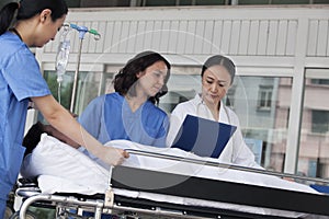 Paramedics and doctor looking down at the medical record of patient on a stretcher in front of the hospital