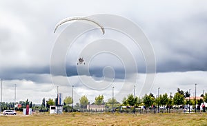 Paramotor with white paraglider flies in the sky over the field on a cloudy day.