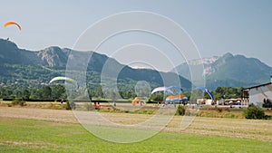 Paraplane lessons in paragliding station in Alps. Athletes taking off on paraglider against blue sky and mountains