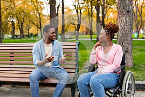 Paraplegic black lady in wheelchair talking to her boyfriend at autumn park