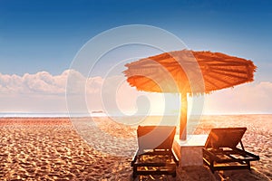 Parasol and sun bed loungers on empty tropical beach at sunset with beautiful warm colors, summer vacation holiday destination