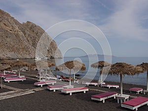 Parasols and empty sun loungers  on the black sand of Perissa Beach.
