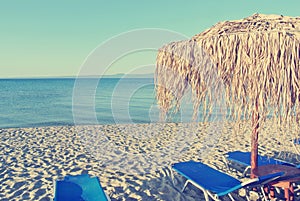 Parasols and sun loungers on white sandy beach; faded, retro style