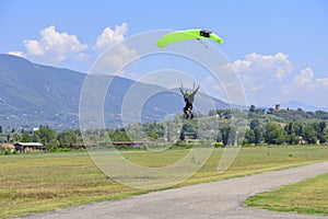 paratrooper with green parachute prepares for landing. On background the blue sky, mountains and green hills