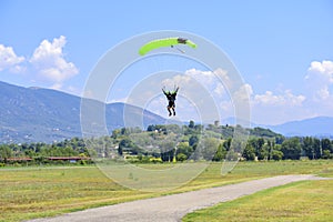 paratrooper with green parachute prepares for landing. On background the blue sky, mountains and green hills