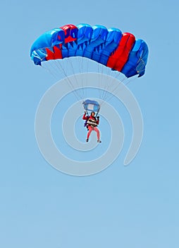 A paratrooper in a red suit descends under the canopy of a parachute