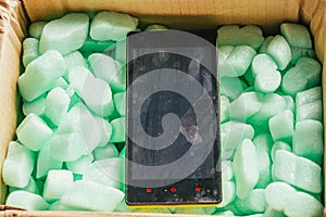 Parcel of online shop, phone in a cardboard box on green styrofoam