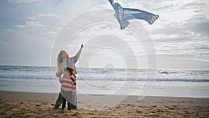 Parent child playing kite on ocean beach weekend. Young single mom helping son