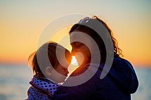 Parent and child are sitting on the beach by the ocean. Camping. Tourism. Mom and daughter admire the sunset on the shore of the