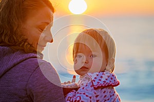 Parent and child are sitting on the beach by the ocean. Mom and daughter admire the sunset on the shore of the winter sea.