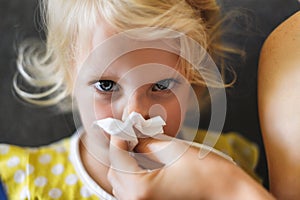 Parent hand helping the little girl to blow her nose with a hygienic wet wipe. Seasonal sickness.