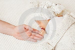 Parent holding Baby Hand. Father Hand and sleeping Newborn. Adorable one month Child lying over White woolen Blanket in Hat