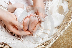 Parent holding in the hands feet of newborn baby. Mother making foot massage for her newborn baby. Mom and her child. Happy Family