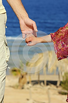 Parent holds the child`s hand on the beach