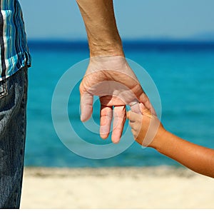 The parent holds the child`s hand on the beach