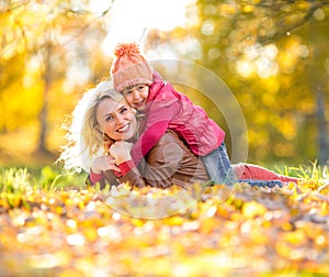Parent and kid lying together on falling leaves in autumn