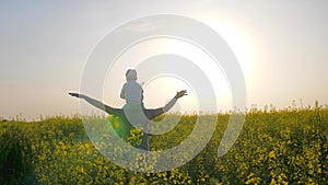 Parent with kid playing airplane on nature, son sits on shoulders father on meadow, happy dad with boy in backlight