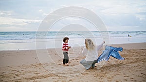 Parent launching kite toy with little boy on beach. Family playing together