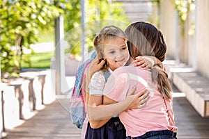 Parent mother taking child to school. Pupil girl of primary school go study with blue backpack outdoors. Back to school. First day