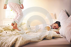 A parent never rests. Shot of a cheerful little girl jumping on the bed to wakeup her sleeping dad at home.