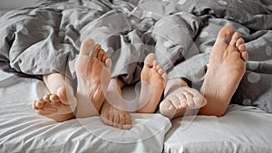 Parent\'s and child\'s feet tapping and wiggling under blanket on a comfortable bed. Concept of family love, bonding,