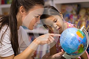 Parent showing a world globe to her kid. Children learning geography