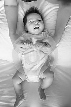 Parent spending time with their laughing baby during playtime on a bed in black and white.