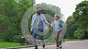 Parent take child to school. Pupil of primary school go study with backpack outdoors. Father and son go hand in hand