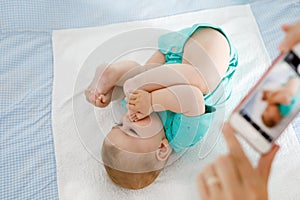 Parent taking photo of a baby with smartphone. Adorable newborn child taking foot in mouth