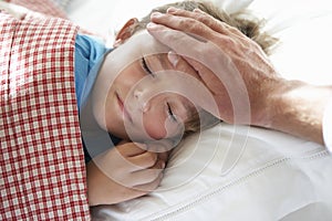 Parent Taking Temperature Of Young Boy Asleep In Bed