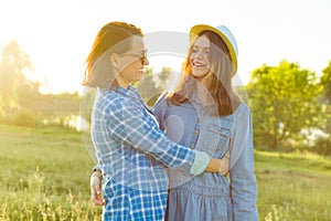 Parent and teenager, mother and 14 year old daughter embrace smiling in nature.